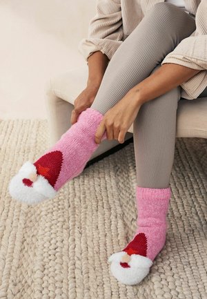 Rosa, fluffiga strumpor med en vit, röd-accentuerad tomteansiktsdesign vid tån. Stickad textur med en vikbar mudd, bärs med grå, ribbade leggings.