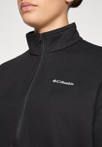 Pullover in pile nero con zip a un quarto, colletto alto e logo Columbia in bianco sul lato sinistro del petto; texture liscia, design aderente.