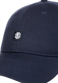 Marineblaue Kappe mit einem gebogenen Schirm, strukturiertem Stoff und einem kleinen schwarzen und weißen Logo-Patch auf der Vorderseite. Mit sichtbaren Nähdetails.