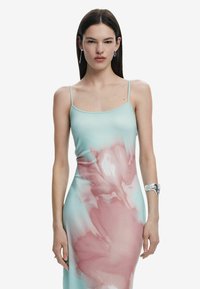 Rochie tip camisole ajustată, de culoare teal deschis, cu un model floral roz. Are bretele subțiri și o textură netedă, moale. Accesoriu din brățară argintie.