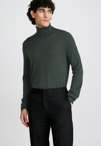 Dark green turtleneck sweater in a ribbed texture, paired with black trousers featuring an elastic waistband and side pockets.