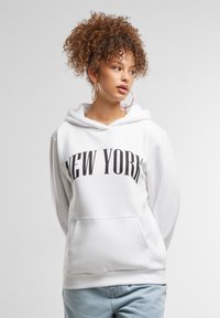 Felpa bianca con cappuccio che presenta la scritta "NEW YORK" in grassetto nero sul petto. Ha una tasca a marsupio e polsini a coste.