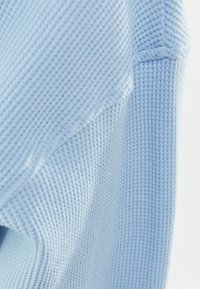 Ljusblått våffelstickat tröja med textilerad yta och ribbade detaljer som ger ett mjukt och mysigt intryck. Inga framträdande detaljer syns.