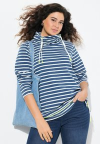 Top a maniche lunghe a righe blu e bianche, con collo a imbuto e coulisse. Presenta una cerniera laterale ed è abbinato a una borsa a tracolla in denim.