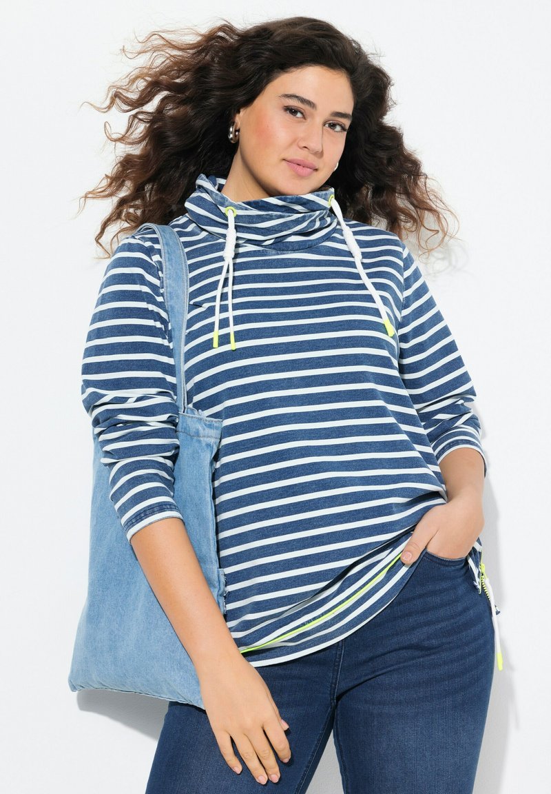 Top a maniche lunghe a righe blu e bianche, con collo a imbuto e coulisse. Presenta una cerniera laterale ed è abbinato a una borsa a tracolla in denim.