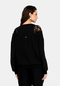 Maglione nero con dettagli in pizzo sulle spalle, vestibilità ampia, orlo e polsini a coste, piccolo logo sul retro. Tessuto morbido con rifiniture texture.