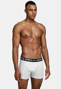 White cotton boxer briefs with a black band displaying "JACK & JONES" text, shown on a male model with a muscular build.