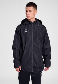 Chaqueta negra impermeable con cremallera frontal, capucha ajustable y detalle de logo. Presenta mangas largas y un corte relajado.