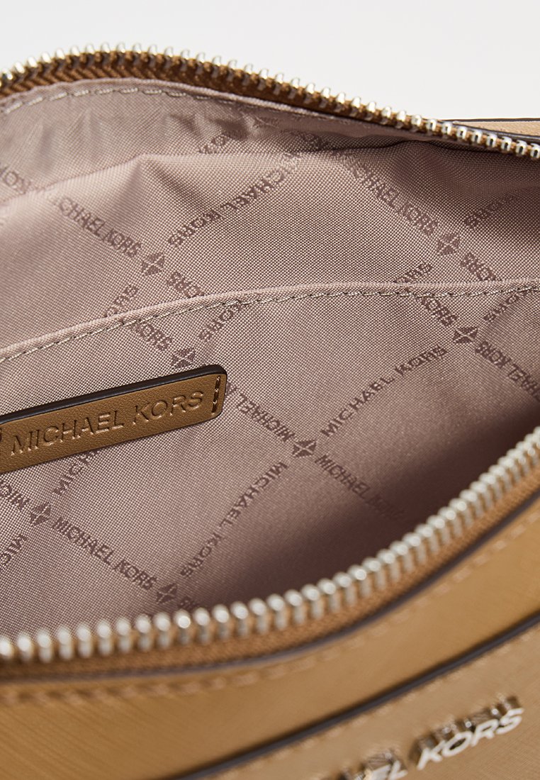 Intérieur de sac à main synthétique marron avec un doublure à motif, présentant une étiquette en cuir estampillée "MICHAEL KORS" et une fermeture zippée.