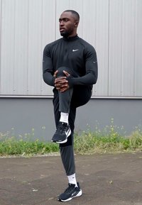 Sportowy strój z dopasowaną czarną bluzą z długim rękawem i zwężającymi się spodniami, noszony z czarnymi sneakersami i białymi skarpetkami, z logo Nike.