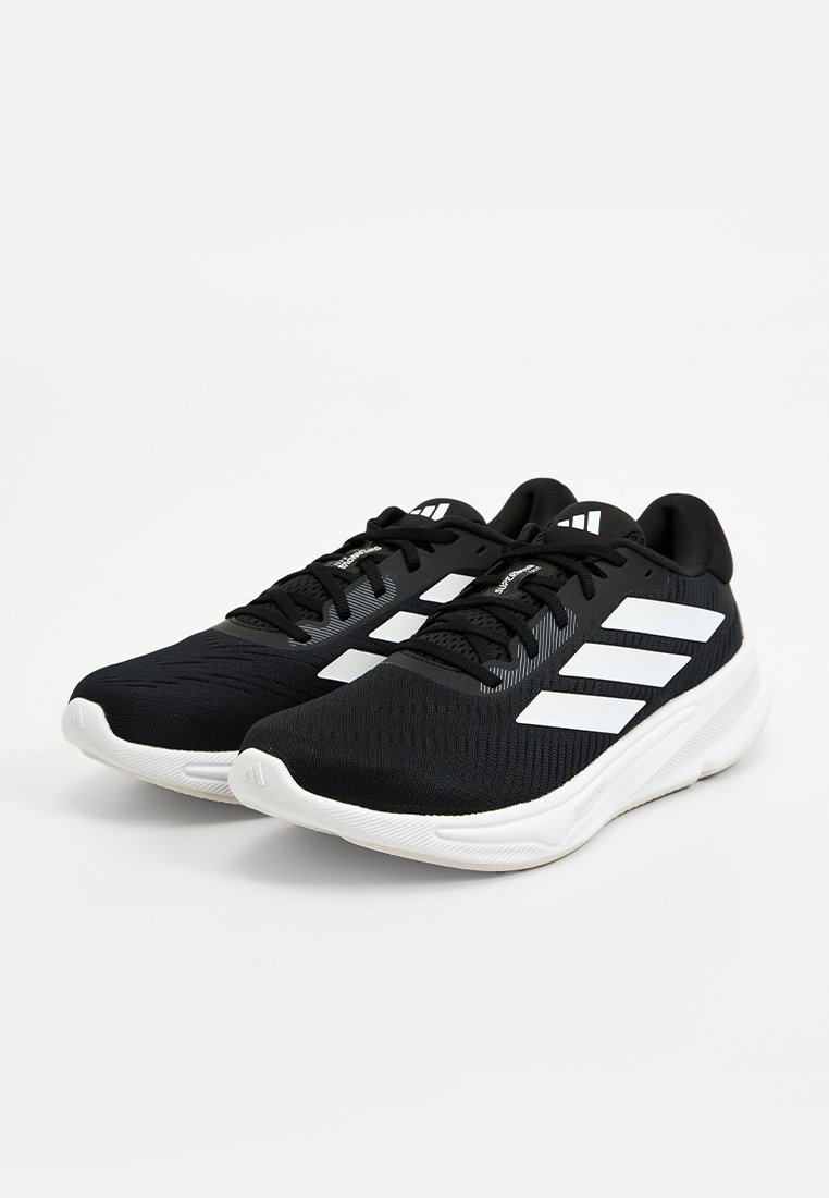 Scarpe da ginnastica nere con tomaia traspirante, tessuto testurizzato, design del logo a tre strisce bianche e suola bianca spessa.