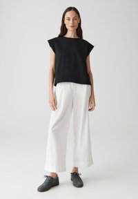 Zwarte top met korte mouwen en textuuraccenten, gecombineerd met losse witte broek en grijze sneakers. Eenvoudig, modern ontwerp met een losse pasvorm.