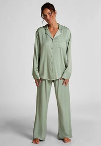 Ljusgrönt pyjamaset i satinmaterial, bestående av en knäppningsbar topp med en ficka och löst sittande, vida byxor.
