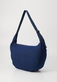 Sacoche en tissu bleu marine avec une structure souple, large bandoulière réglable et fermeture à glissière pour un accès facile au contenu.