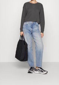 Felpa grigia a taglio corto con texture a coste, jeans dritti azzurro chiaro, borsa tote nera trapuntata e scarpe da corsa grigio-argento.