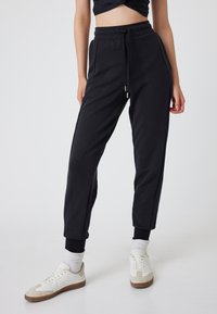 Pantalones deportivos negros con cinturilla elástica, cordón y bolsillos laterales. Presentan puños acanalados y una textura suave y lisa.
