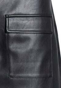Prenda de cuero negro con un bolsillo rectangular y costuras visibles. La textura es suave con un ligero brillo.