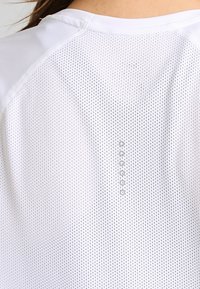 Top deportivo blanco de malla con escote redondo y cinco pequeños botones circulares en la espalda, destacando su transpirabilidad y comodidad.