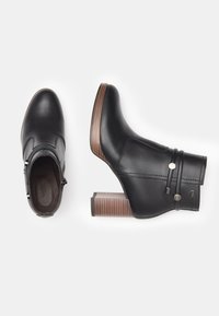 Stivale alla caviglia in pelle nera con un tacco alto in legno texturizzato, caratterizzato da due cinghie decorative e una cerniera laterale per una facile calzata.