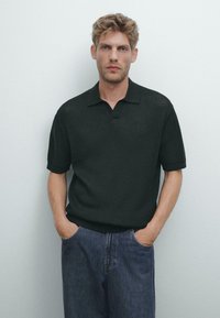 Mörkgrön t-shirt med kort ärm, i ribbat tyg, med en notched krage och en avslappnad passform, ihop med blå denimjeans.