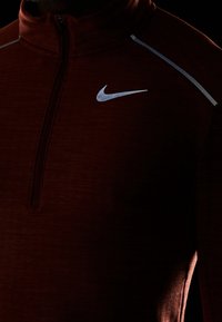 Dunkelmauronefarbenes Quarter-Zip-Sportoberteil mit reflektierendem silbernen Nike-Swoosh-Logo und reflektierendem Streifen auf der Schulter.