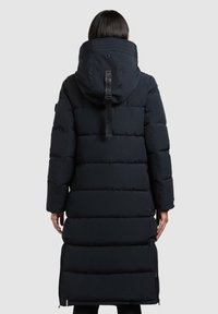 Abrigo acolchado largo negro con un cuello alto y capucha ajustable. Presenta costuras horizontales, cremalleras laterales y un lazo de marca en la parte posterior.