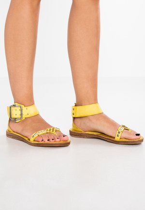 Sandales en cuir jaune avec bride de cheville à boucle, semelle plate, clous décoratifs et bandes texturées. Design ouvert à l'avant avec un style décontracté.