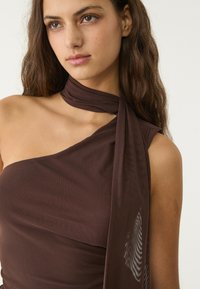 Top marrone a spalla unica realizzato in tessuto leggero, presenta un design drappeggiato con un lungo numero di sciarpa fluttuante. Dettagli di superficie testurizzati visibili.