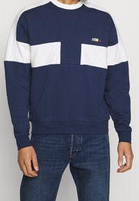 Mörkblå sweatshirt med vita horisontella ränder. Har en rundad nacke och två framfickor. Tillverkad av en mjuk bomullsblandning.