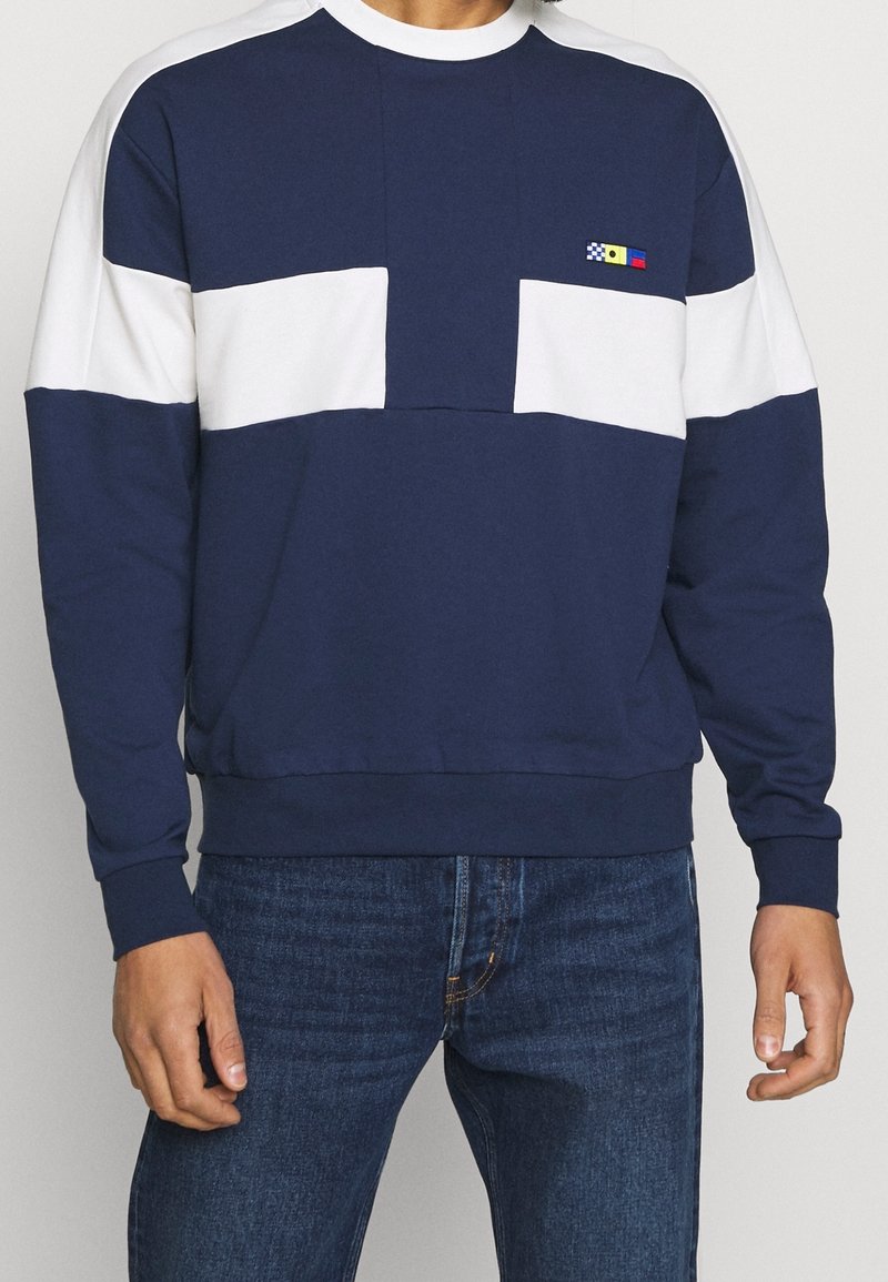 Mörkblå sweatshirt med vita horisontella ränder. Har en rundad nacke och två framfickor. Tillverkad av en mjuk bomullsblandning.