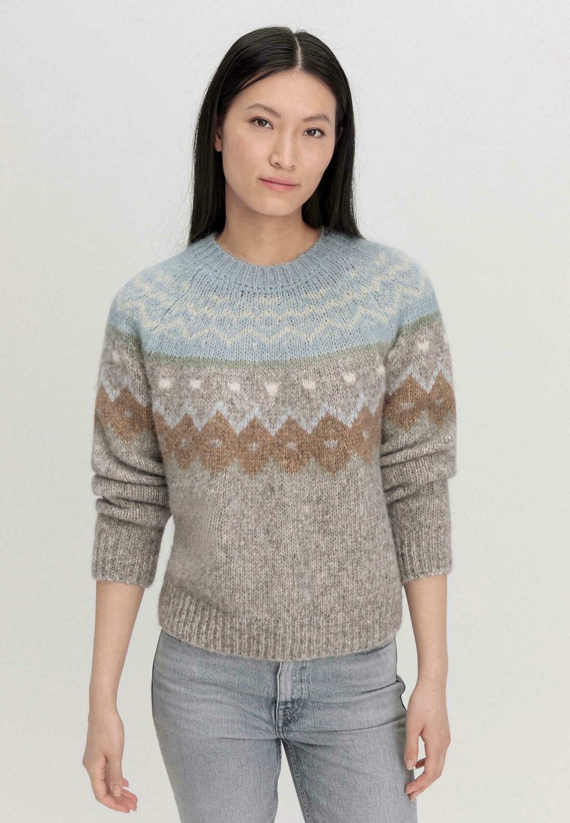 Neulepusero vaaleassa beigeessä, jossa on monivärinen kauluskuvio; sisältää vaaleansinisiä, ruskeita ja kermaisia yksityiskohtia; ribatut hihansuut ja helma.