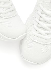 White sneakers made of breathable mesh fabric, featuring a textured pattern, flat laces, and a rounded toe with a smooth rubber sole.