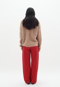 Suéter marrón esponjoso y pantalones rojos anchos vistos desde atrás, con texturas suaves y un ajuste holgado. Footwear negro es visible.