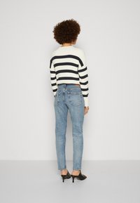 Striped knit sweater in white and navy, cropped design. Paired with light blue slim-fit jeans, featuring back pockets. Simple black heels.