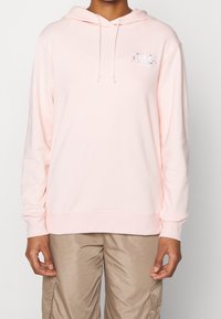 Sudadera con capucha en rosa claro con cordón ajustable, con un diseño floral y un logo de Adidas en blanco en el pecho. Textura de tela suave.