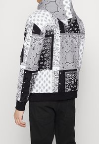 Hoodie i svart och vitt, med ett bandana-mönster och varierande texturer. Inkluderar ribbad nederkant och ärmslut.