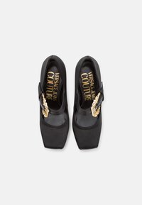 Czarne satynowe szpilki z kwadratowym noskiem, z akcentem w postaci złotego elementu i wytłoczonym logo na wkładce.