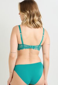 Reggiseno in pizzo teal con spalline regolabili e chiusura a gancio, abbinato a mutandine teal coordinate, caratterizzate da una superficie in microfibra liscia.