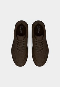 Σκουρόκαφέ vegan αθλητικά παπούτσια με κορδόνια, διάτρητη περιοχή στη μύτη και μαξιλαρωμένους περιμετρικούς γιακάδες, παρουσιασμένα από πάνω σε απλό ανοιχτό φόντο.