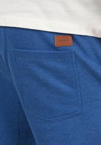 Blaue Sweatpants aus strukturiertem Stoff, mit einer Gesäßtasche und einem braunen Lederpatch mit der Aufschrift "BLEND", gestickte Details entlang der Kanten.
