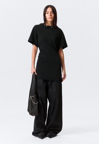 T-shirt preto oversized com mangas curtas, apresentando um ajuste justo na cintura. Combinado com calças largas pretas e uma bolsa preta com detalhes em corrente.