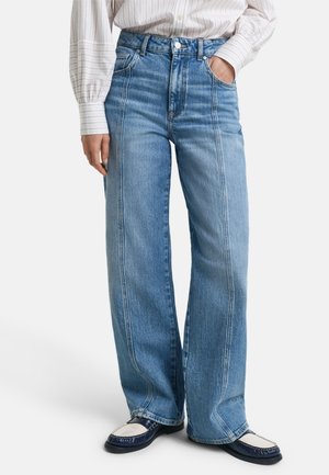 Jeans de tiro alto en azul claro con un corte holgado, que presentan costuras laterales y un sutil efecto de desgaste. Combinados con unos mocasines azul oscuro y una blusa a rayas.