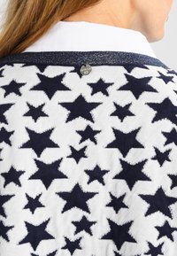 Marineblauwe trui met sterpatroon op een witte achtergrond. Zachte textuur, ronde halslijn en zilveren detail aan de achterkant.