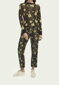 Top negro de manga larga con un patrón floral amarillo; combinado con pantalones florales negros; modelo usando zapatillas beige; textura de tela suave.