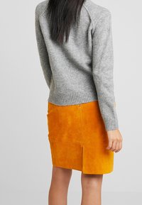 Un pull en laine gris avec un ourlet côtelé, associé à une jupes crayon en daim orange avec une fente au dos et des détails de couture.