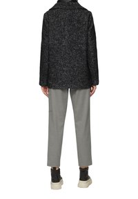 Abrigo de espiga en negro y gris con cuello de muesca, llevado sobre pantalones gris claro y botas negras de tobillo con suelas gruesas.