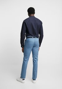 Tmavě modrá košile s dlouhým rukávem spárovaná se světle modrými kalhotami, vyrobená z bavlny s hladkou texturou, s jednoduchým designem bez viditelných vzorů.