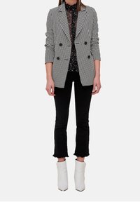 Svart och vit houndstooth dubbelknäppt blazer över en svart blus med prickar, kombinerad med svarta jeans med fransar och vita ankelstövlar.