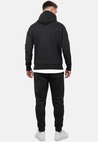 Felpa nera con collo alto e tasca a marsupio, abbinata a pantaloni tuta neri con polsini elasticizzati e tasche laterali.