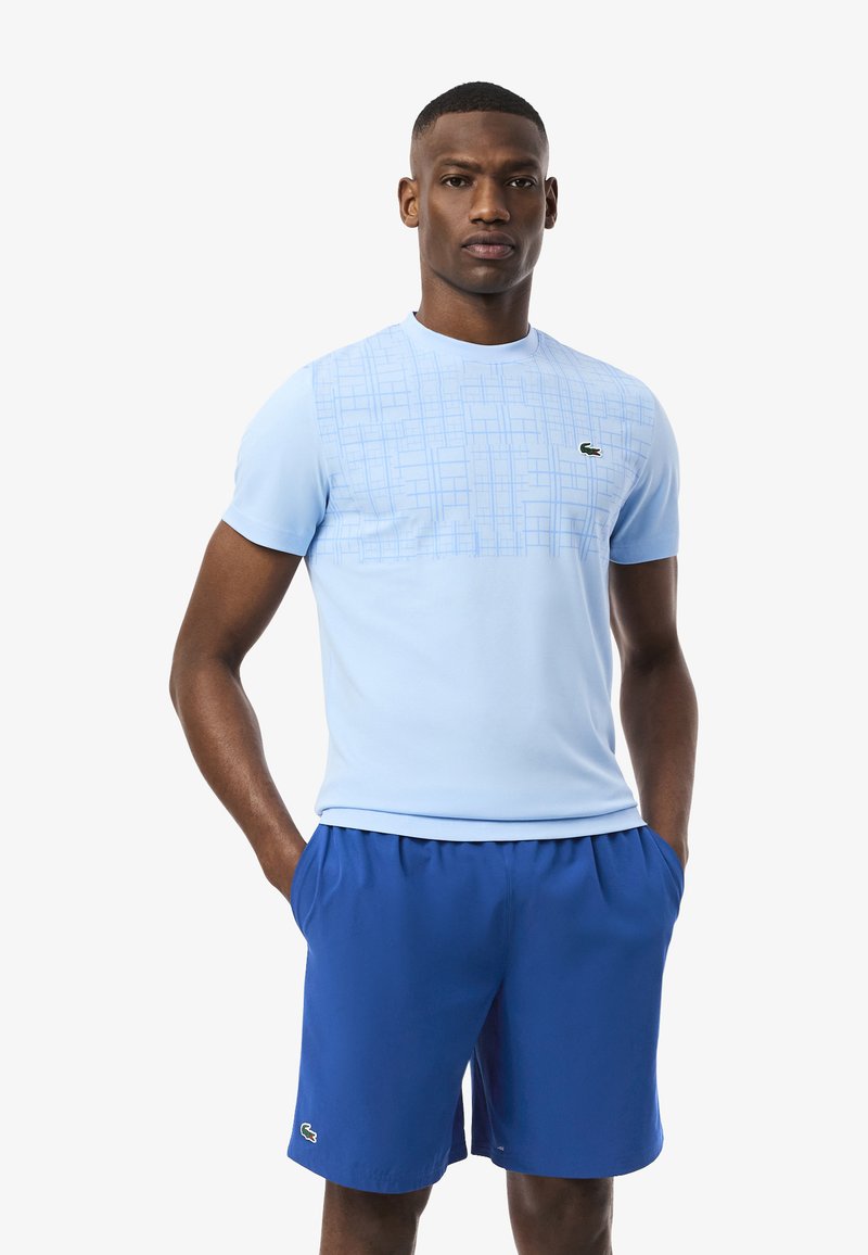 Maglietta sportiva azzurro chiaro con un motivo a griglia nella parte superiore, abbinata a pantaloni shorts blu. Entrambi realizzati in un tessuto liscio e traspirante.